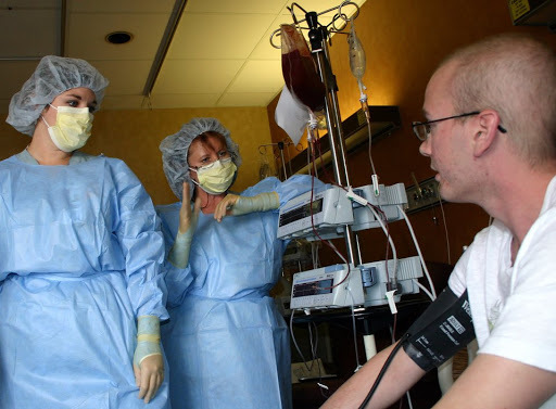 (two doctors in personal protective equipment talking to a cancer patient)