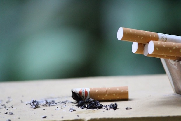 A cigarette butt with more cigarettes on the edge of an ashtray