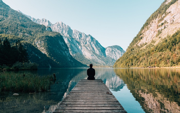 Person sitting on dock by the water looking at mountains