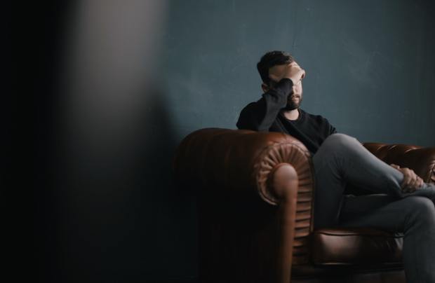 A man sitting on a couch, holding his head