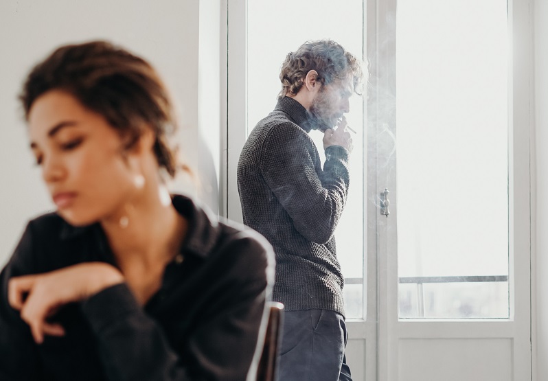 woman sitting in a chair and man smoking in the background