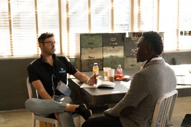 Two men talking, while one makes notes