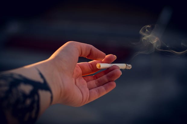 a hand holds a smoking cigarette